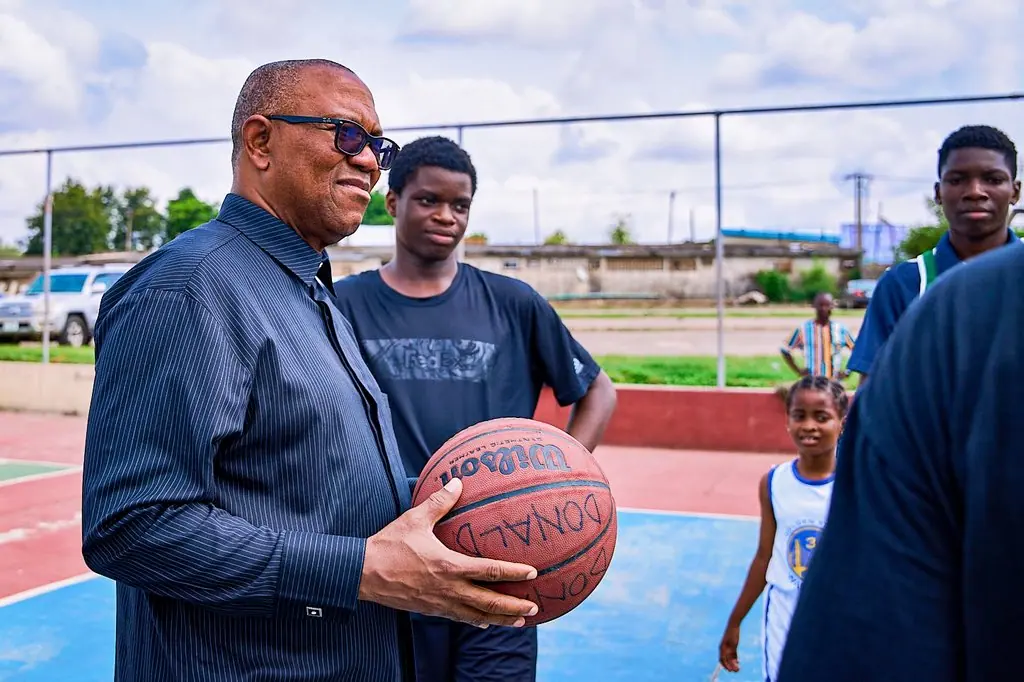 Peter Obi standing on an outdoor basketball court holding a ball, young players around him
