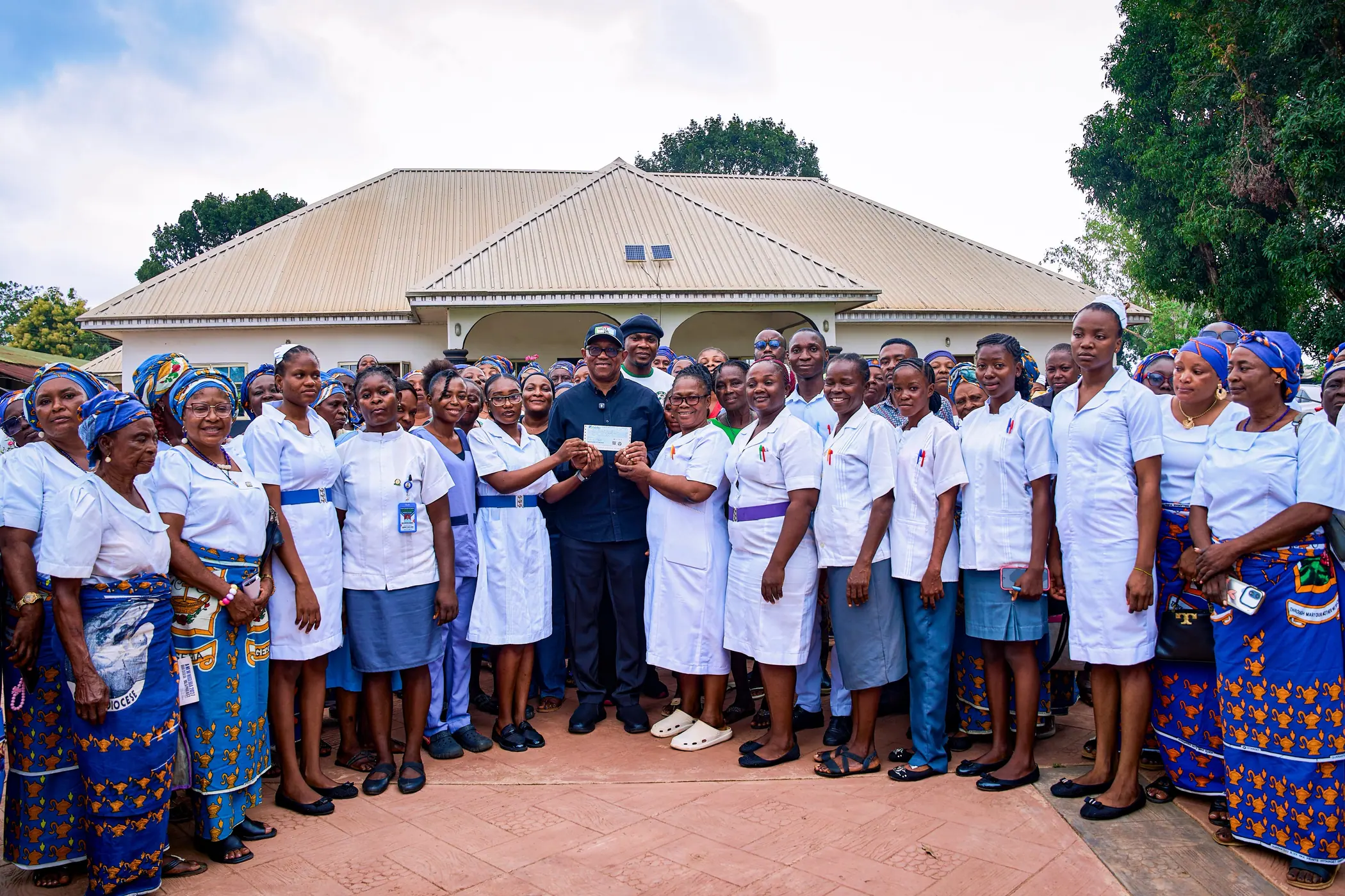 Wide view of Peter Obi presenting a cheque to hospital staff in a courtyard lined with women in blue and white