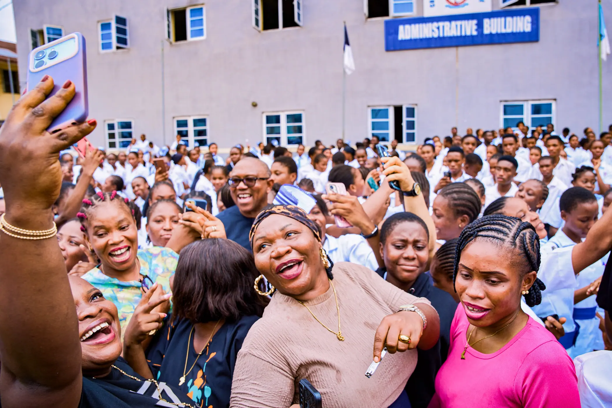 A dense crowd of student nurses raising phones towards Peter Obi outside an administrative building