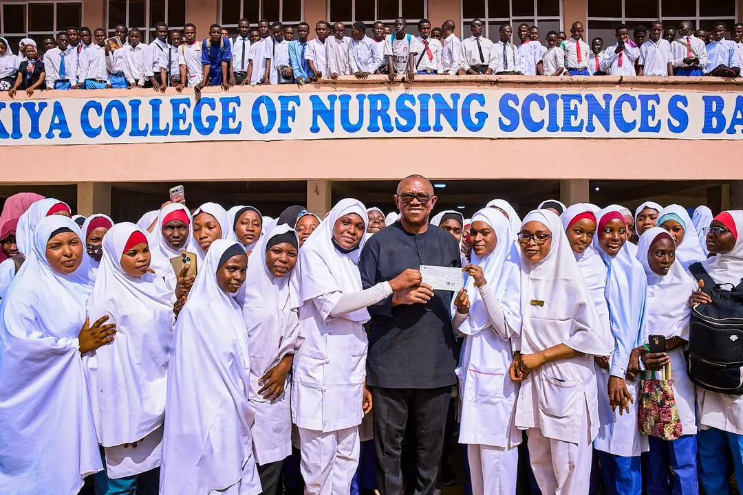 Peter Obi presenting a cheque to students in white hijabs outside a College of Nursing Sciences