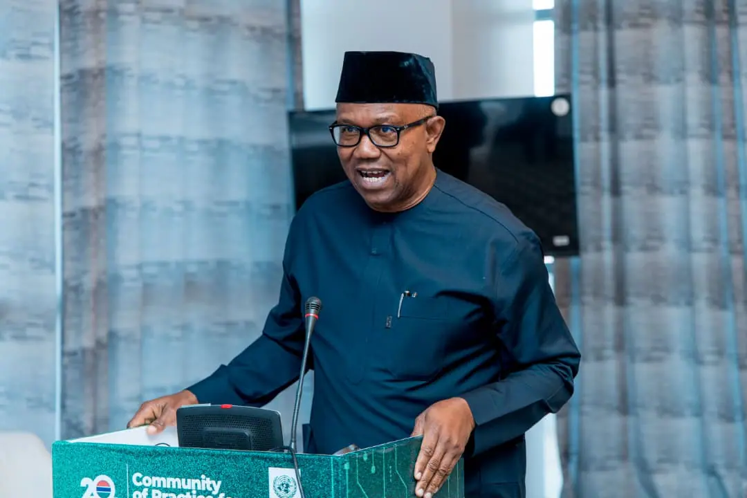 Peter Obi speaking at a green lectern marked Community of Practice, wearing a black cap