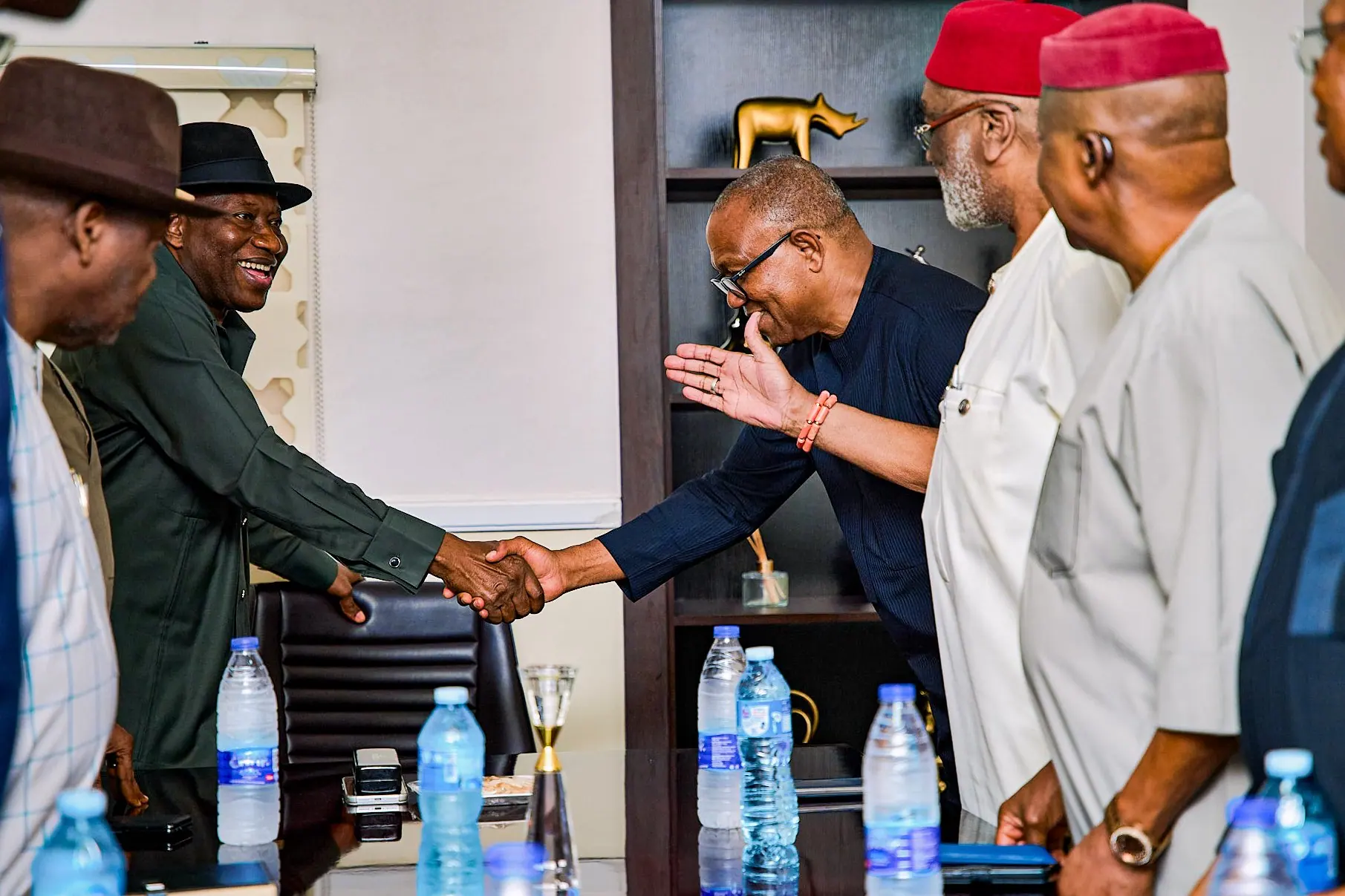 Peter Obi bowing slightly to shake hands across a table, elders in red caps looking on
