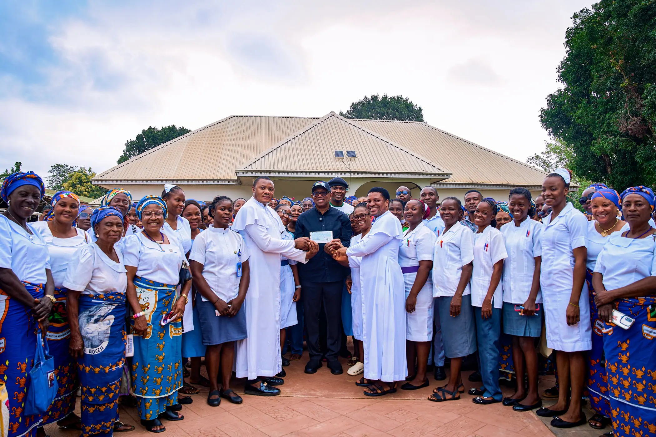 Peter Obi presenting a cheque in a paved courtyard flanked by two rows of women in blue and white