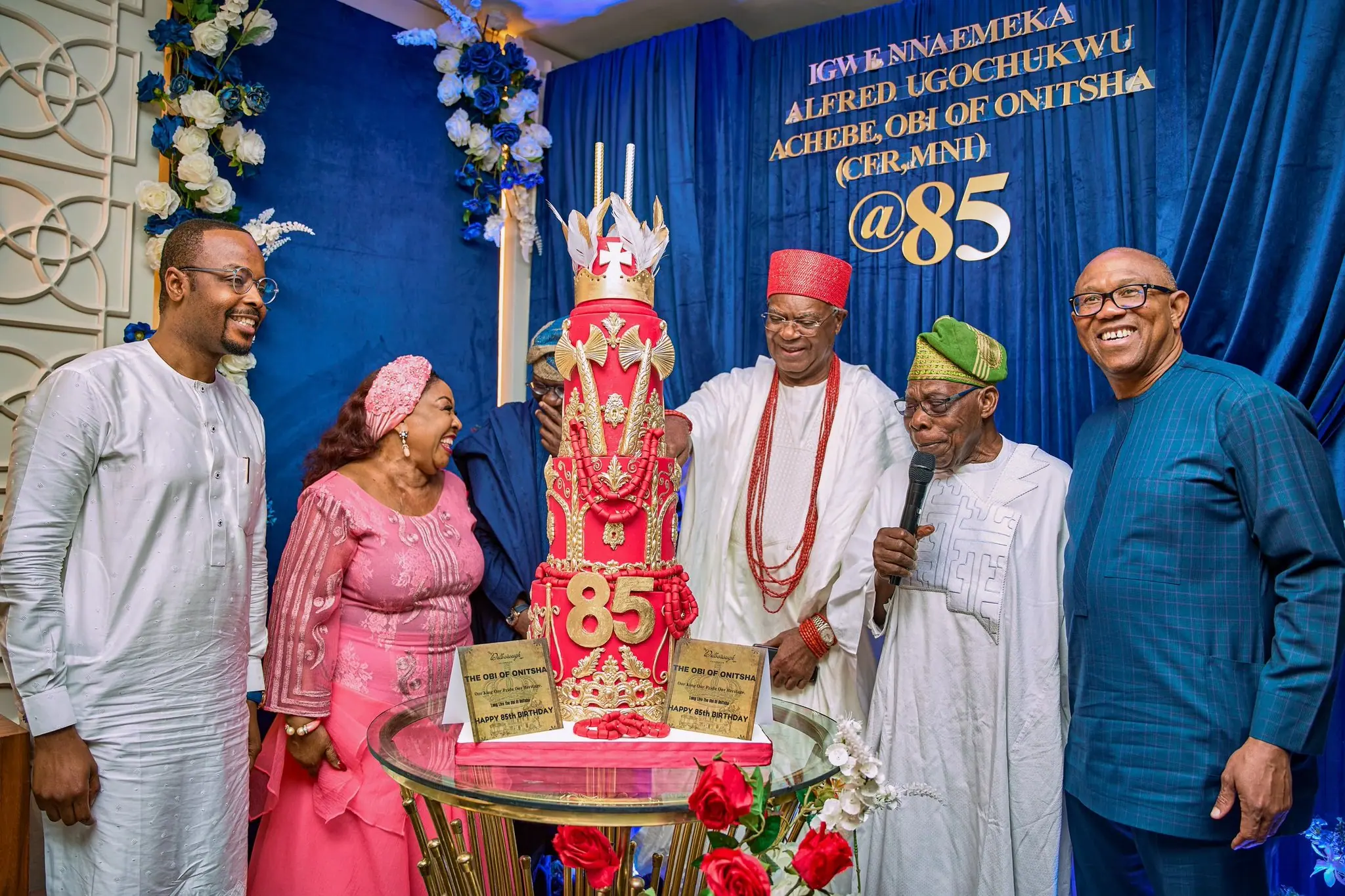 Peter Obi standing with a traditional ruler and guests behind a tall red and gold birthday cake