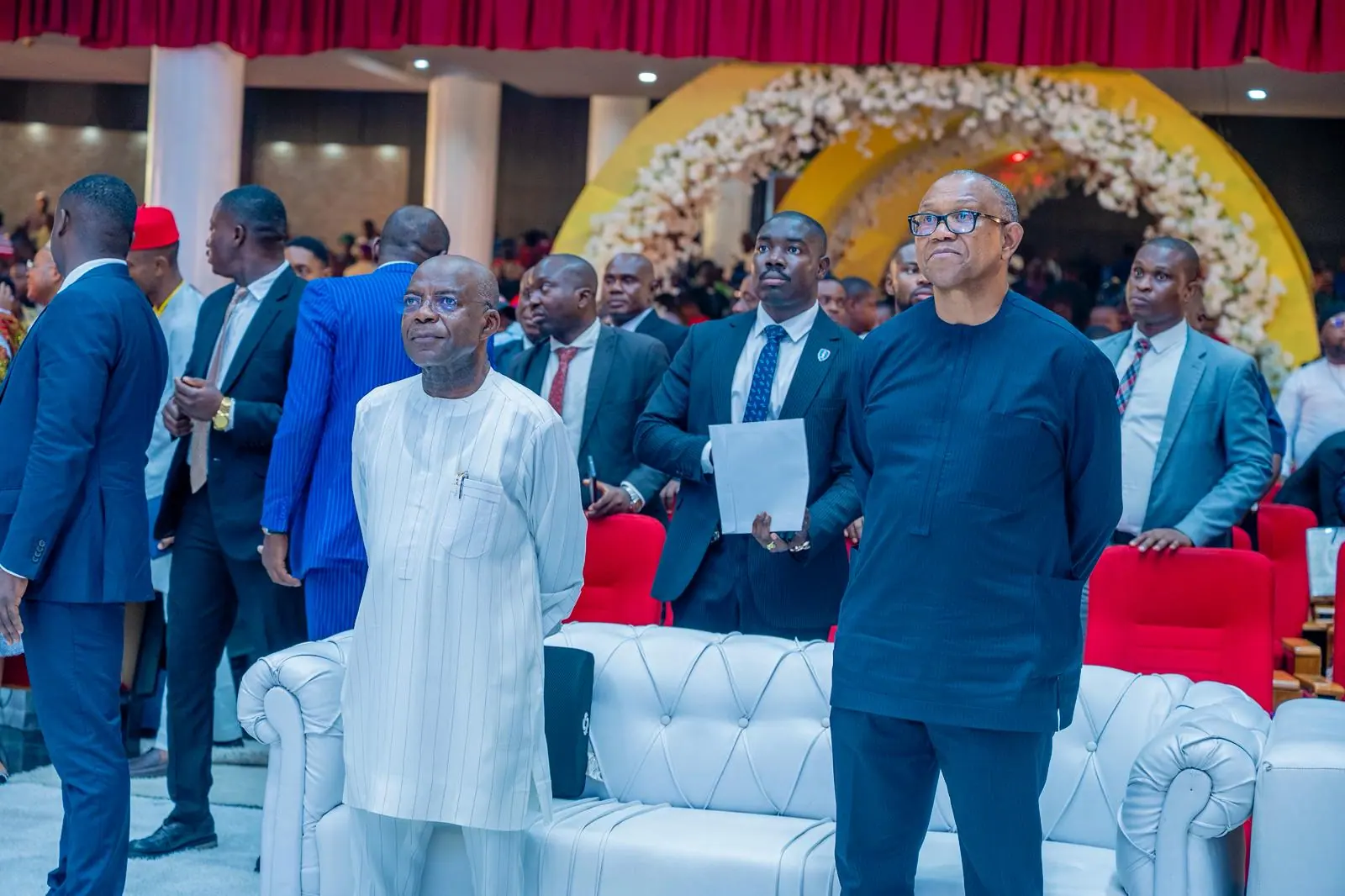 Peter Obi standing with guests in front of a large floral arch at a funeral service