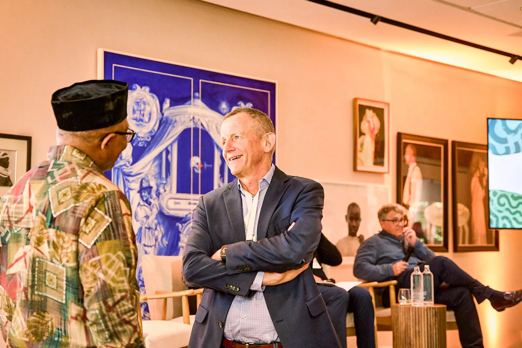 Peter Obi in conversation with a man in a room hung with paintings and drawings