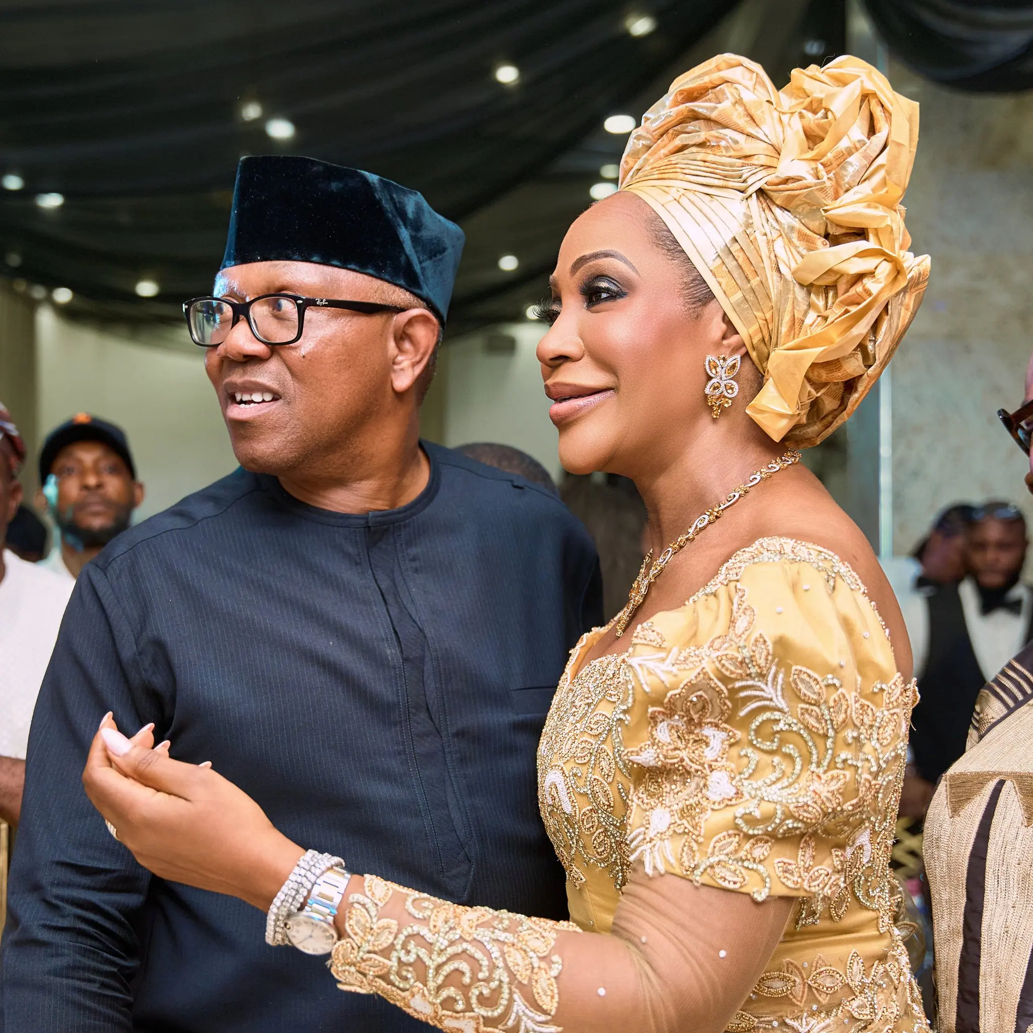 Peter Obi in a black cap standing close to his wife Margaret Obi in a gold gele and gold lace