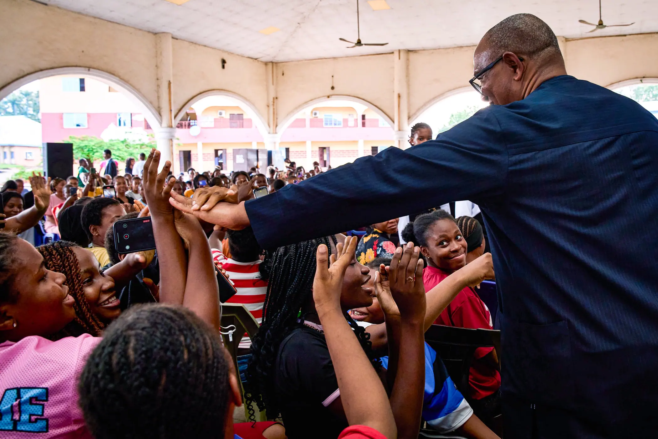 A packed hall of young people with phones and raised hands as Peter Obi reaches across to them