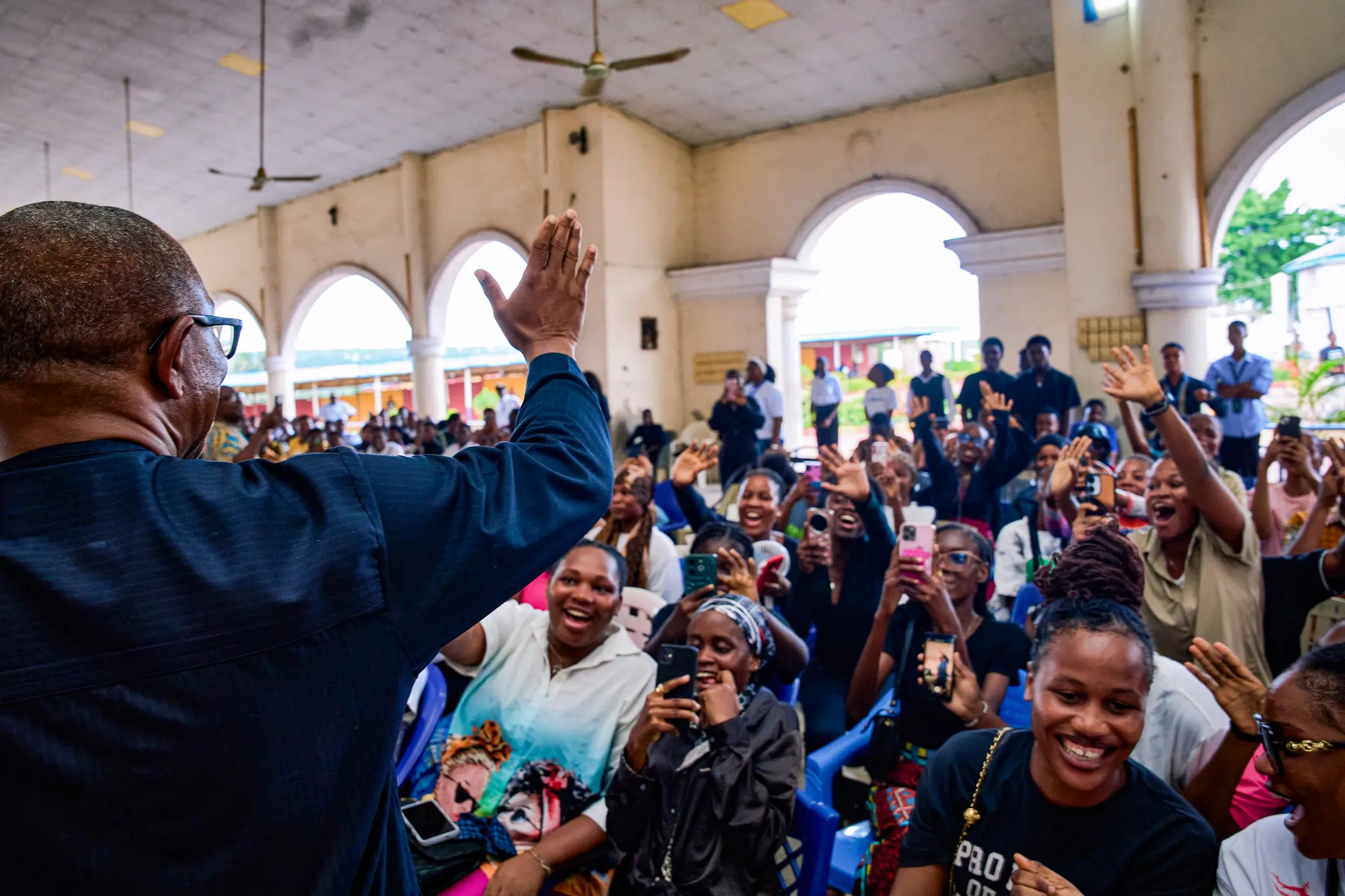 Peter Obi leaning across a barrier to touch the hands of a crowd of young women in a hall