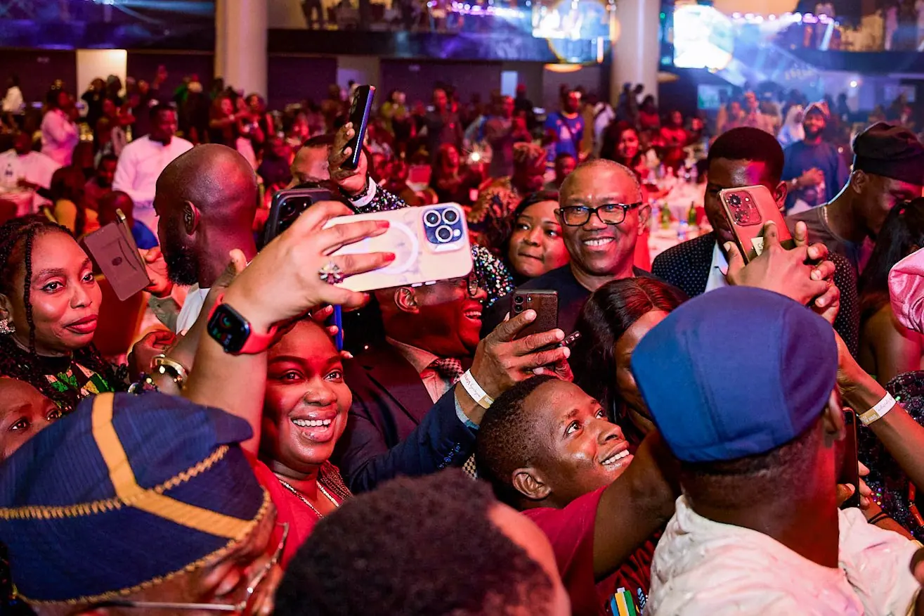 Guests at a banquet hall standing on chairs and holding phones over their heads towards Peter Obi