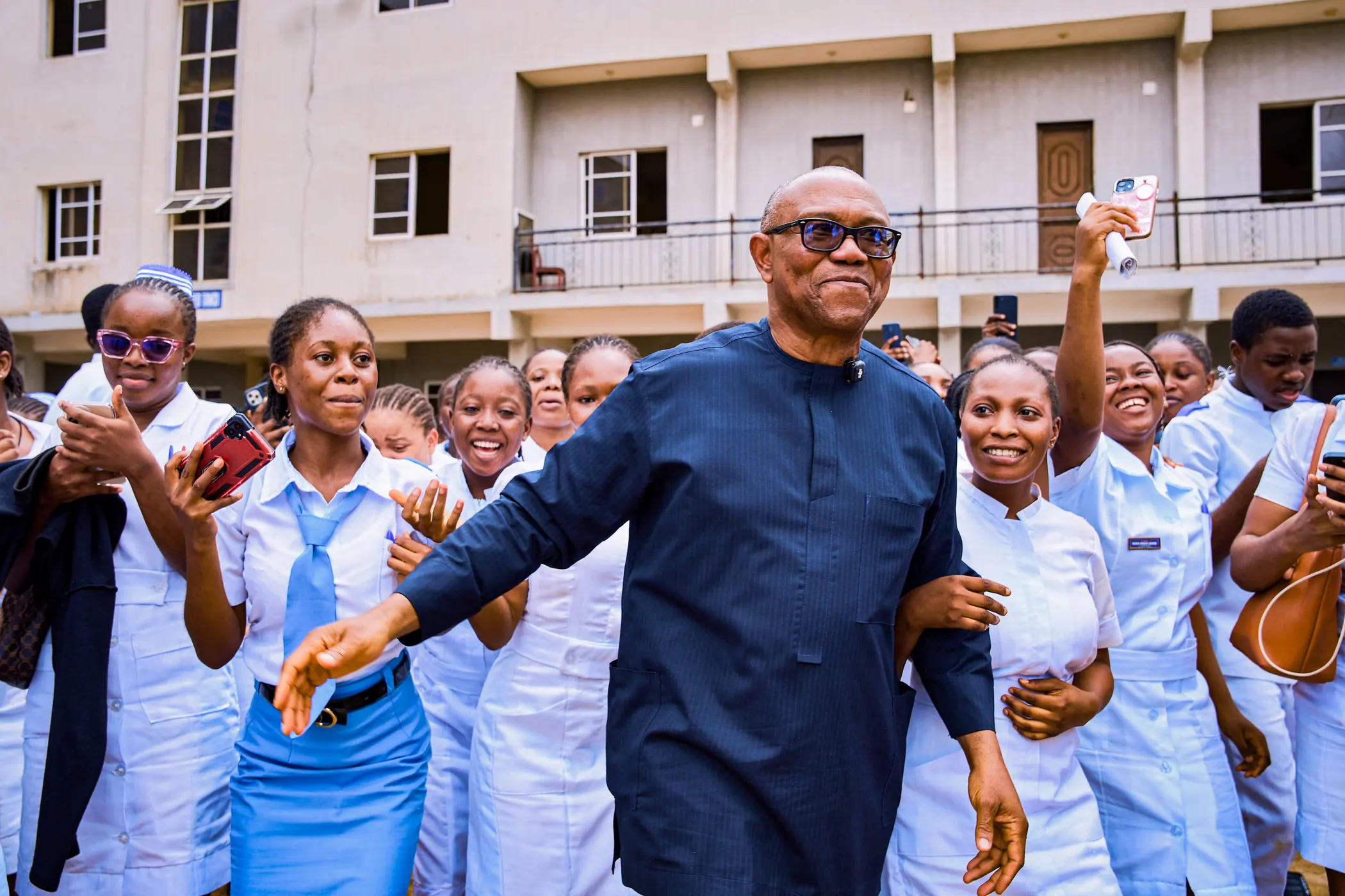 Peter Obi walking through a courtyard of student nurses in white uniforms, arms out on both sides