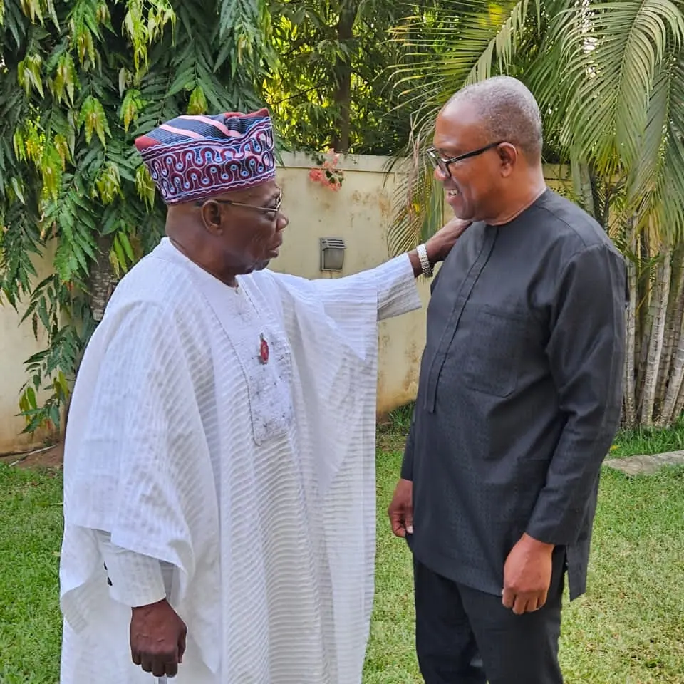 Olusegun Obasanjo in a white agbada and cap, a hand on Peter Obi's shoulder, the two of them talking in a garden