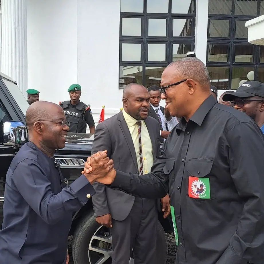 Governor Alex Otti clasping hands with Peter Obi outside a building, aides and police behind them