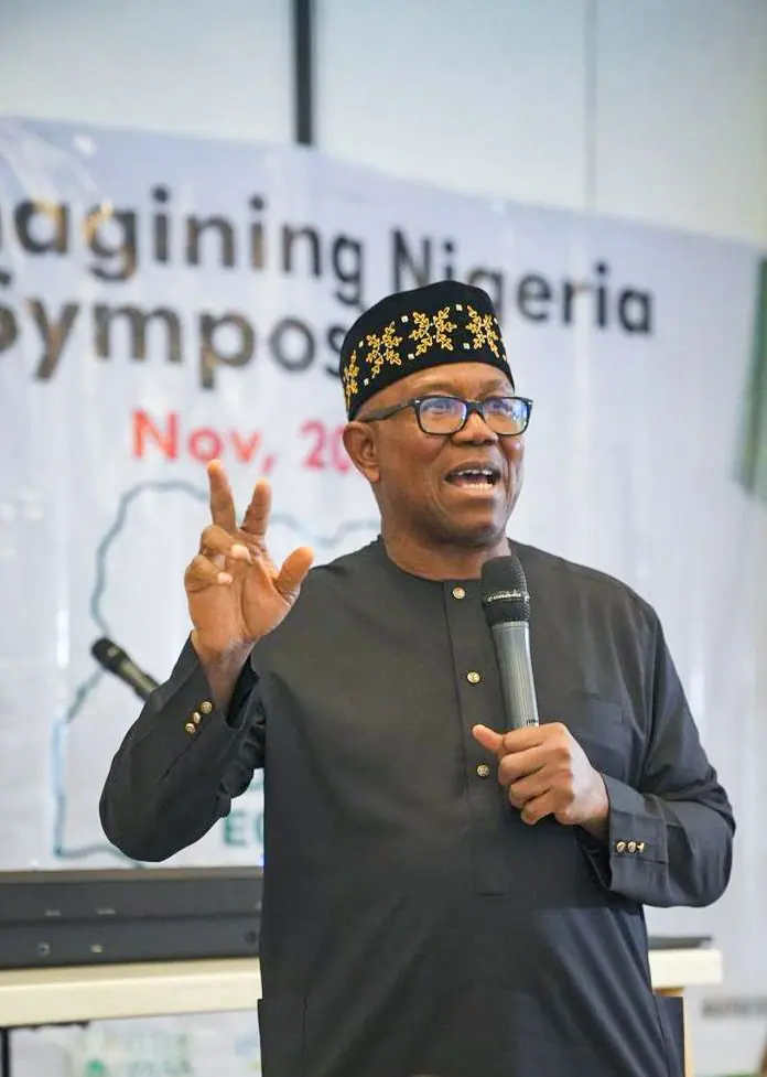 Peter Obi speaking with a microphone and a raised hand in front of a banner reading Reimagining Nigeria Symposium