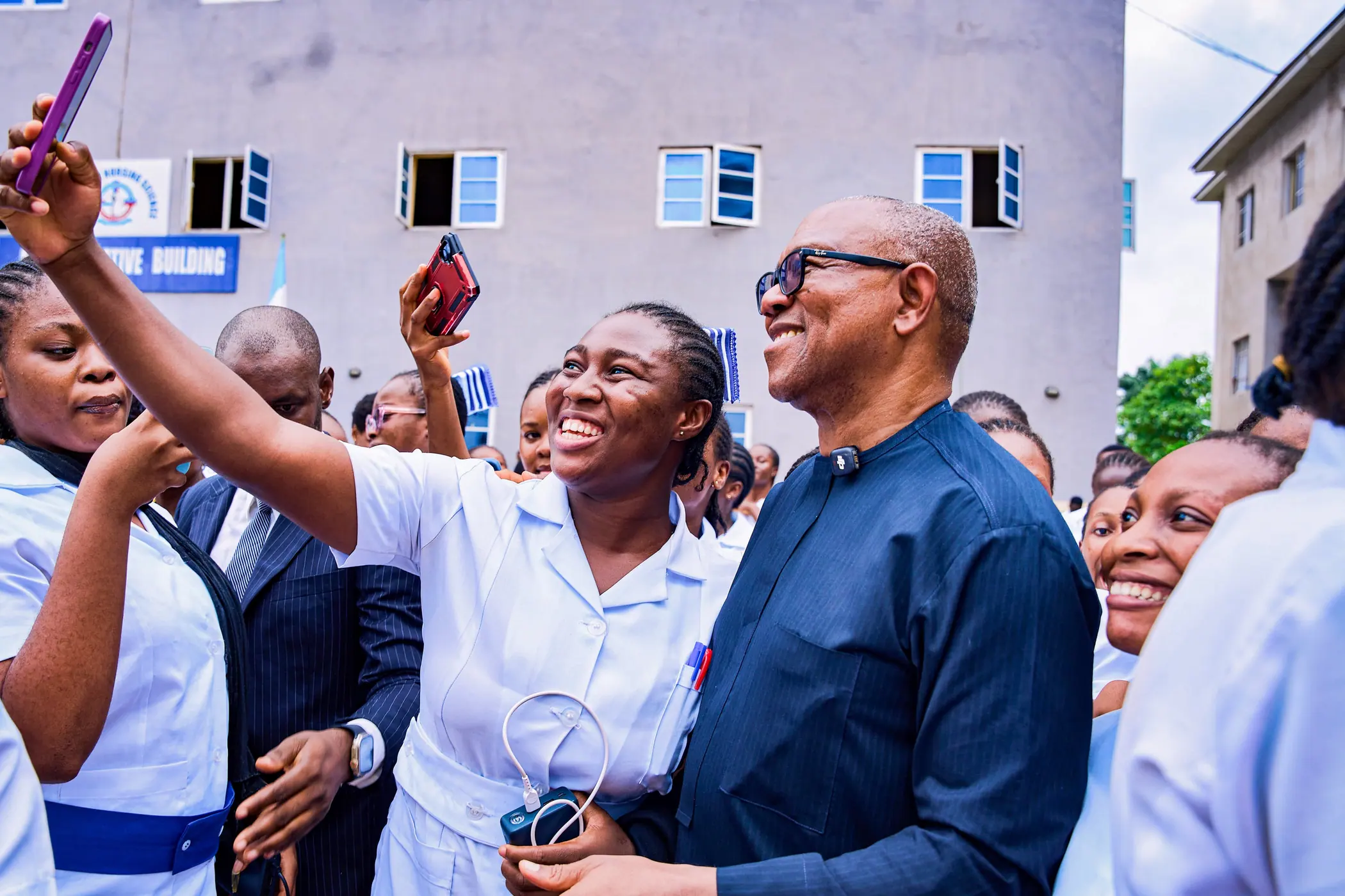 A student nurse in uniform taking a selfie with Peter Obi in a college courtyard