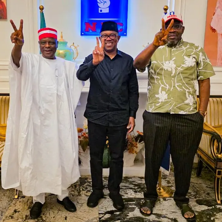 Peter Obi standing between two men on a wet courtyard, all three making a victory sign
