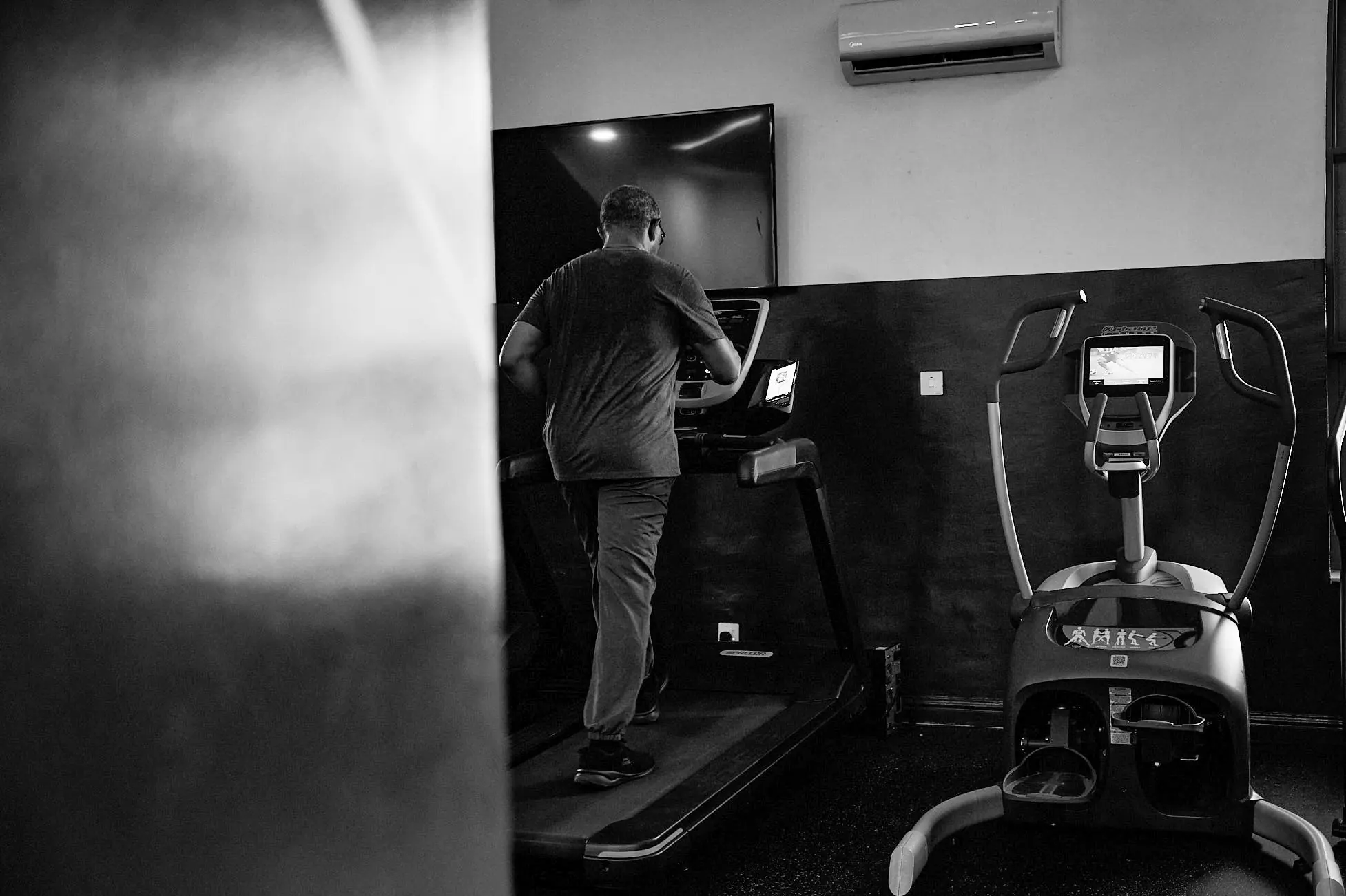 Black and white photograph of Peter Obi walking on a treadmill in a small gym at night