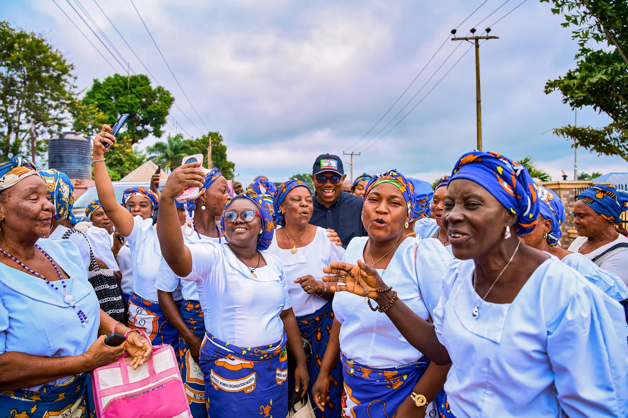 A large group of women in matching blue and white wrappers and headties crowding around Peter Obi