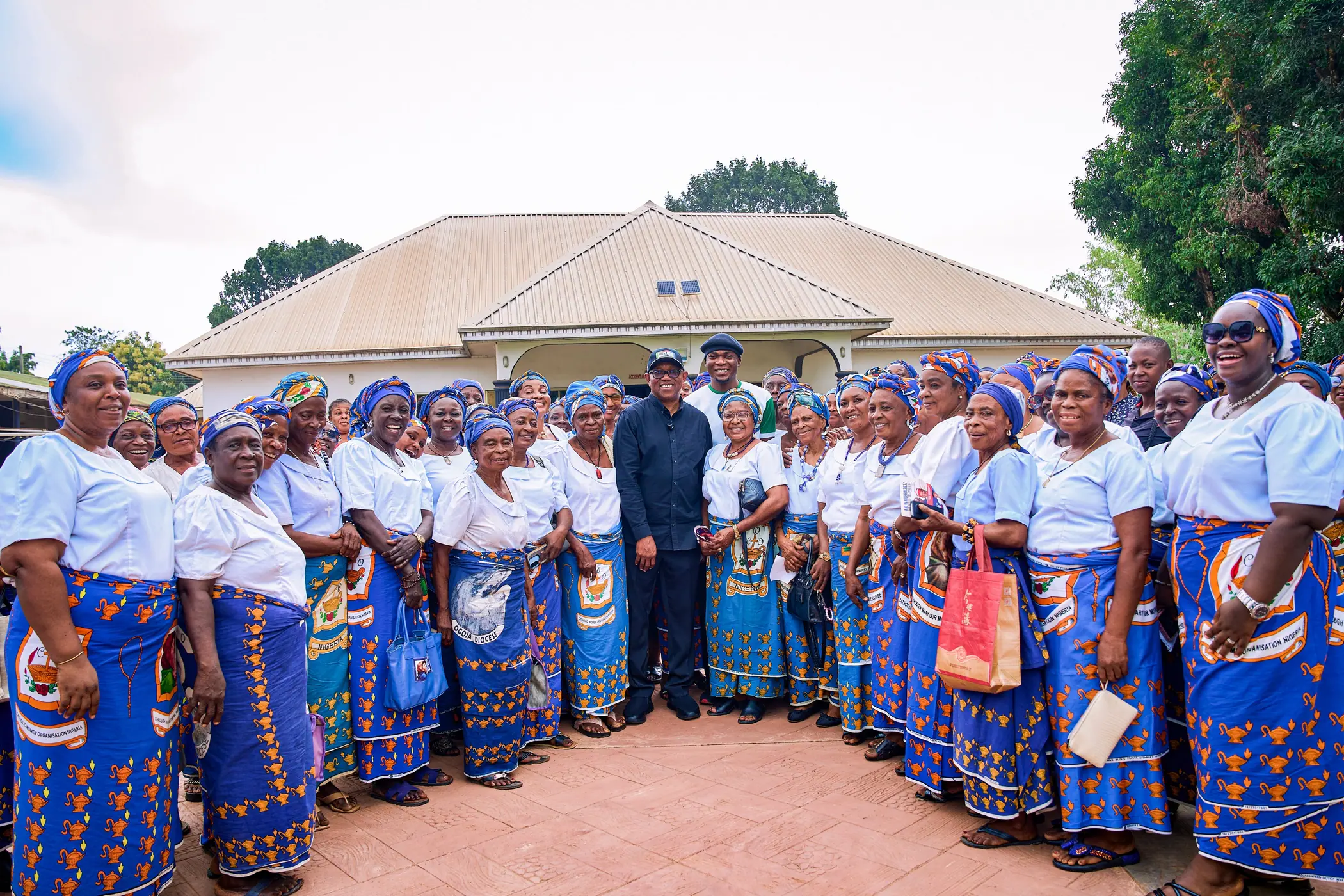 Peter Obi standing at the centre of a hundred women in matching blue and white outside a health facility