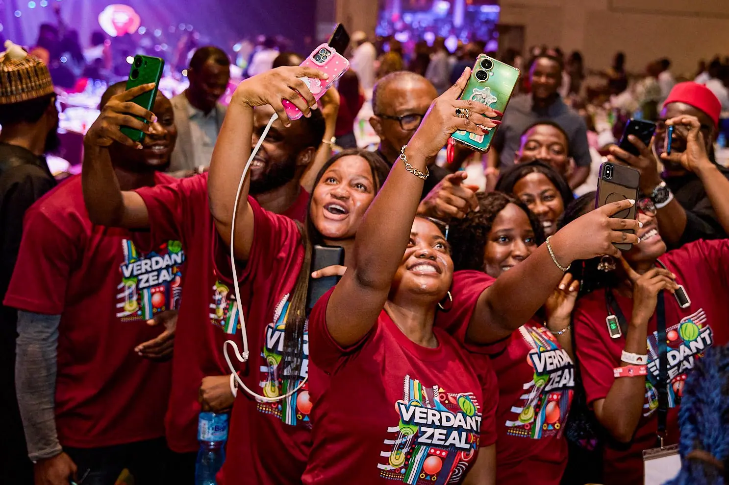 A crowd of young people in matching maroon shirts holding phones up around Peter Obi
