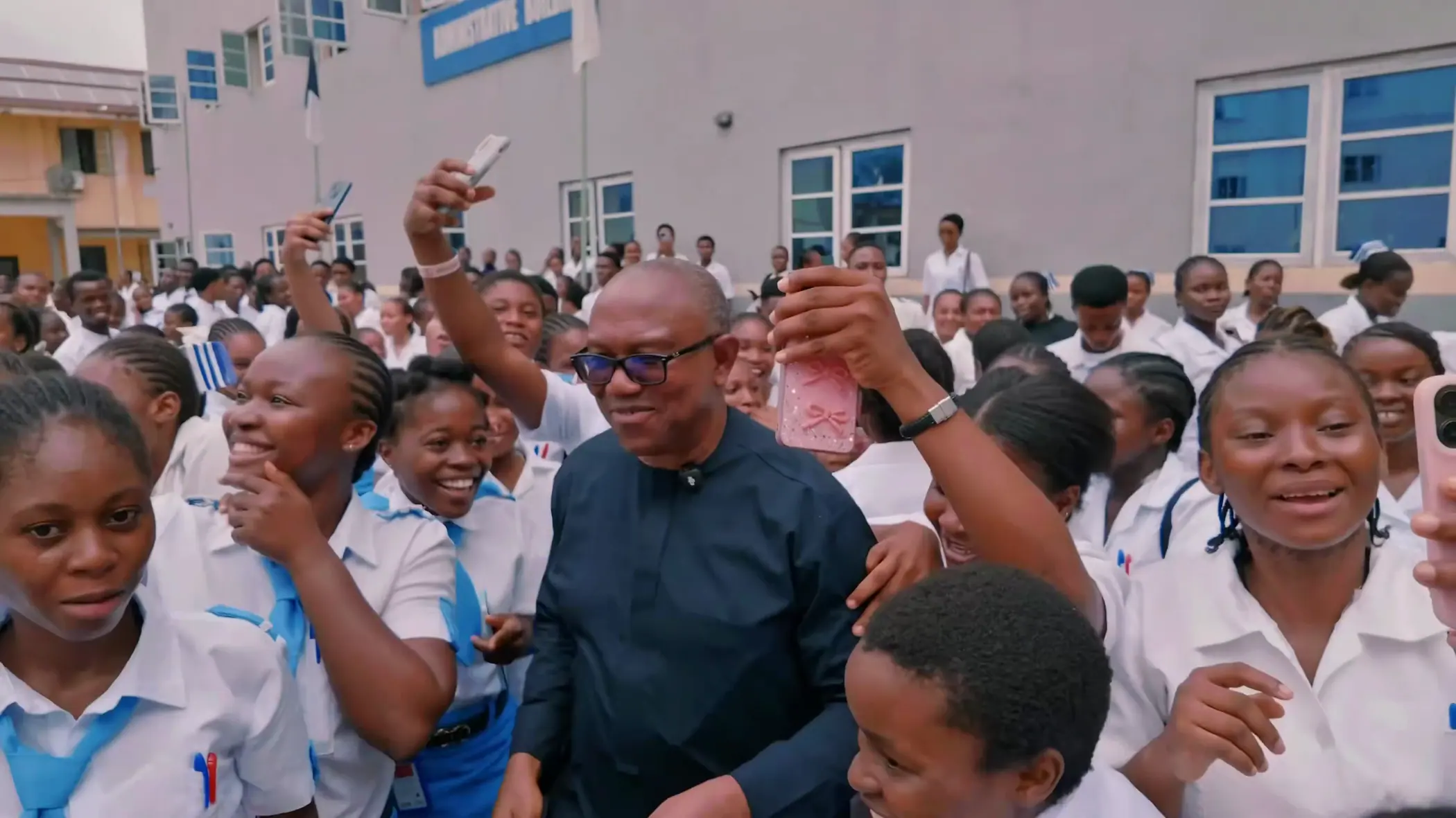 Student nurses in white uniforms cheering around Peter Obi in a college courtyard
