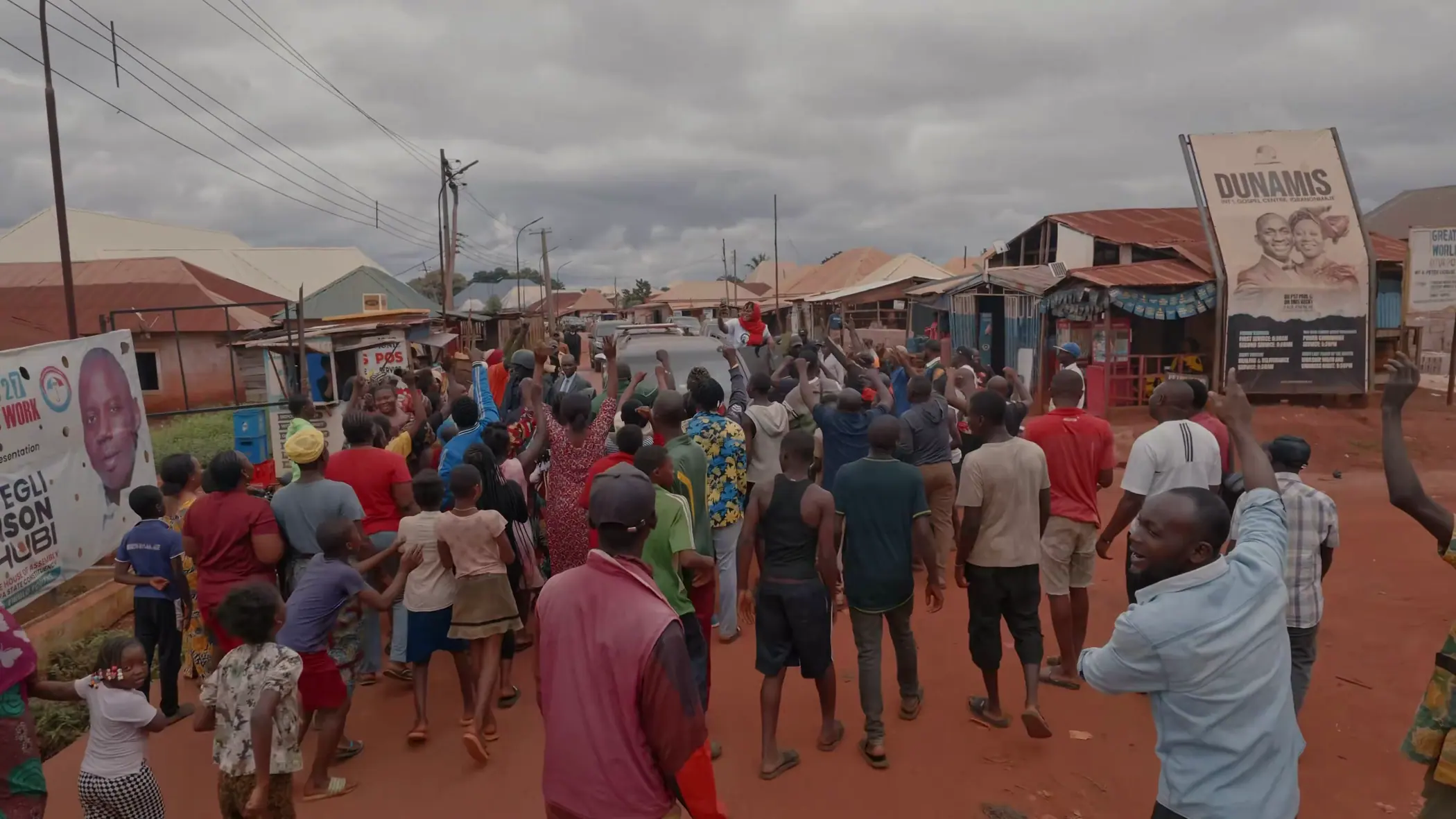 A street packed with people, hands and phones raised, as a vehicle moves slowly through